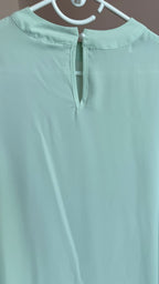 Light green blouse on a hanger against a neutral background