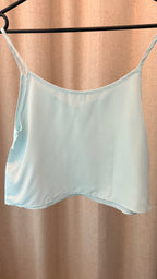 Light blue satin camisole on a hanger against a beige curtain background