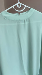Light green shirt on a hanger against a neutral background