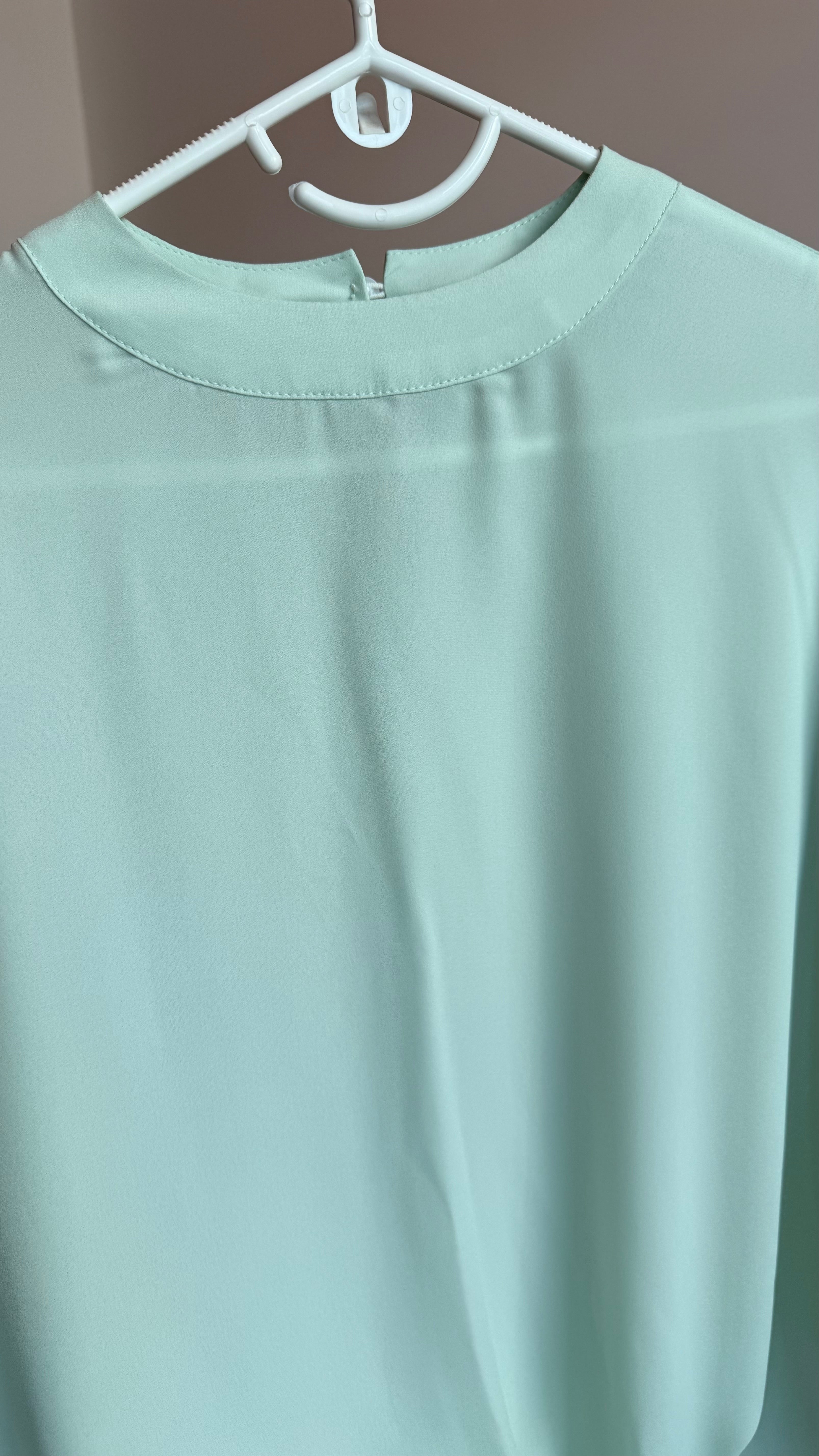 Light green shirt on a hanger against a neutral background