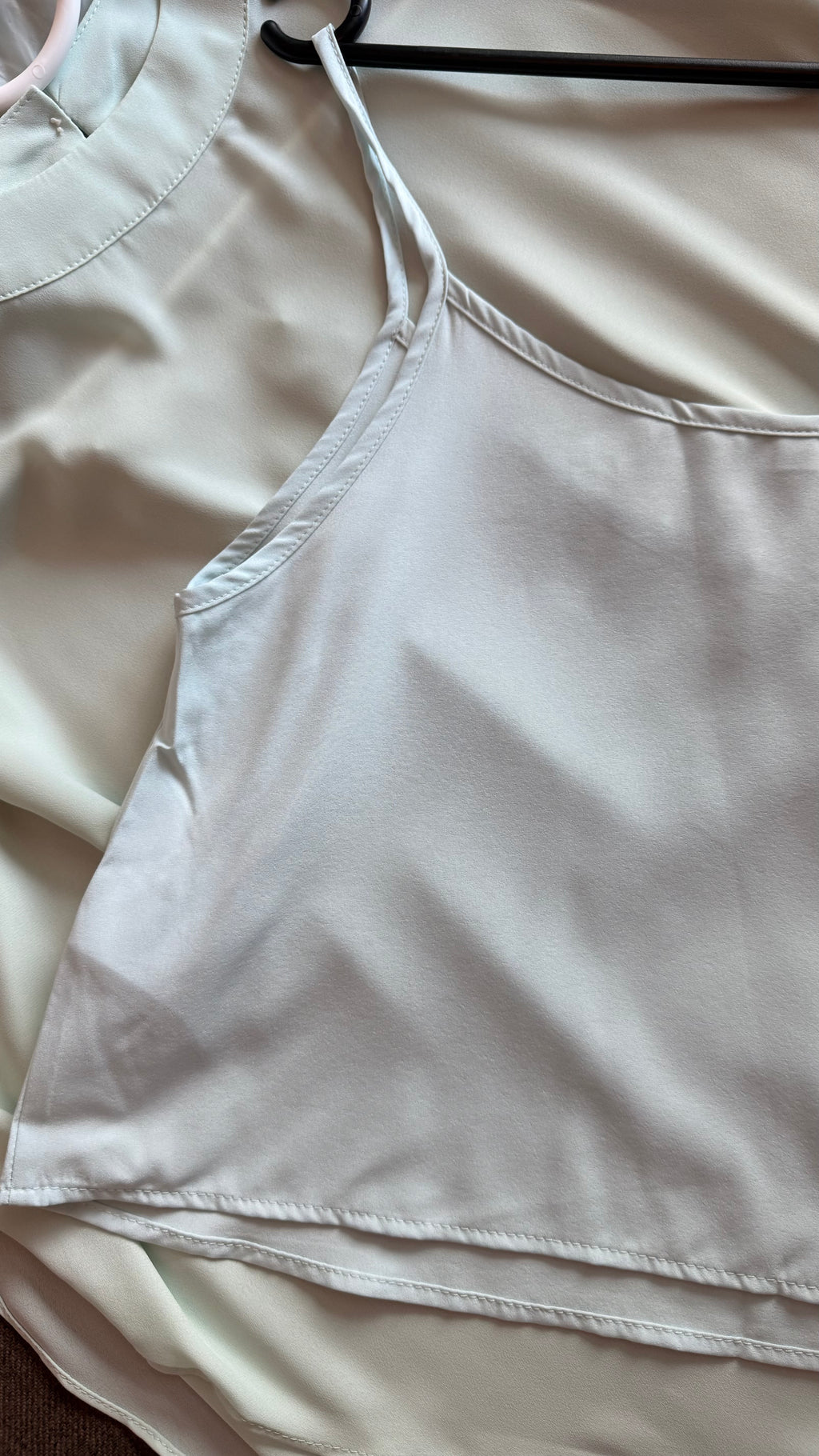 Light-colored top on a hanger with a plain background