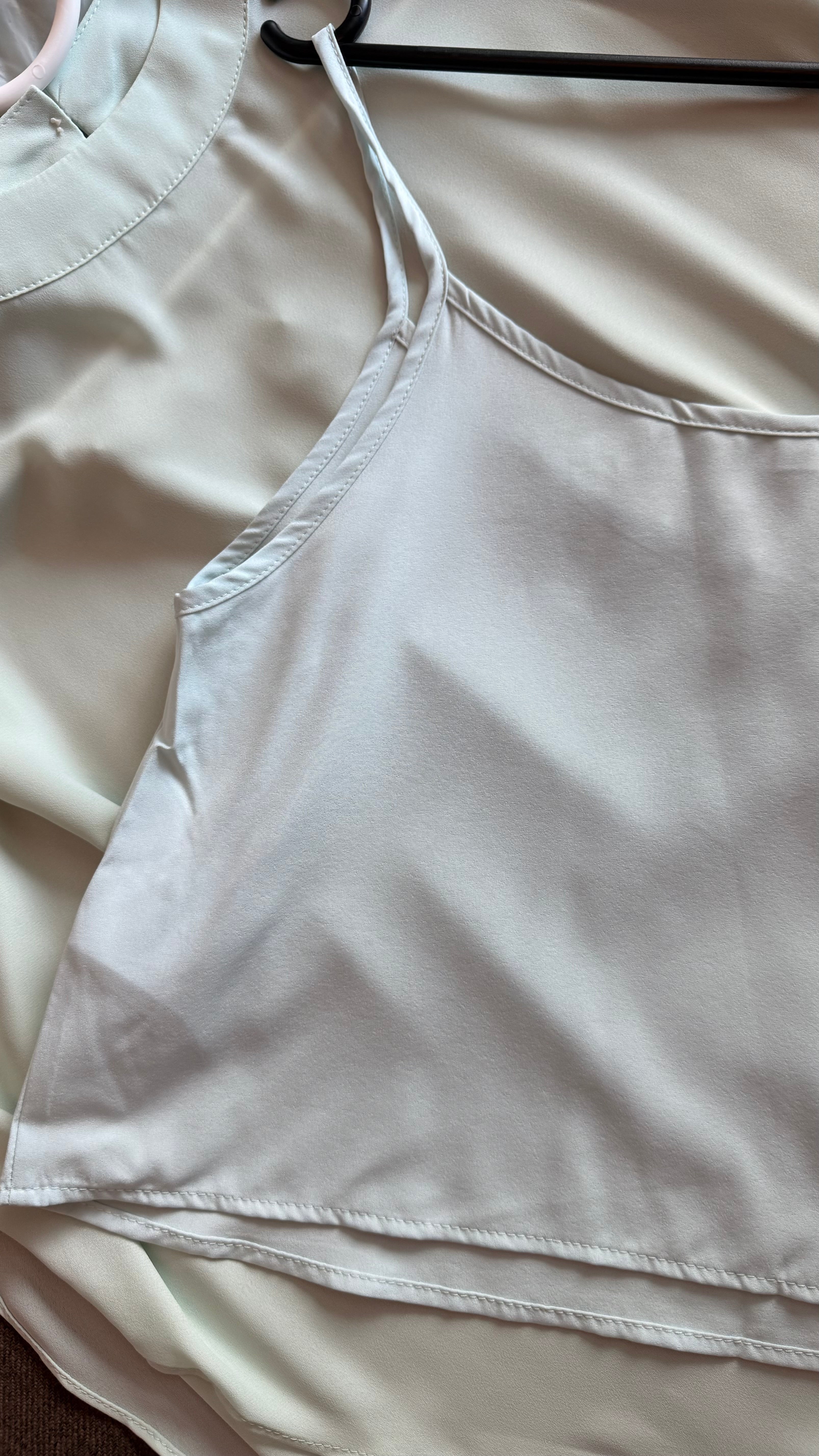 Light-colored top on a hanger with a plain background