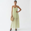 Woman wearing a light green dress holding a straw bag on a white background