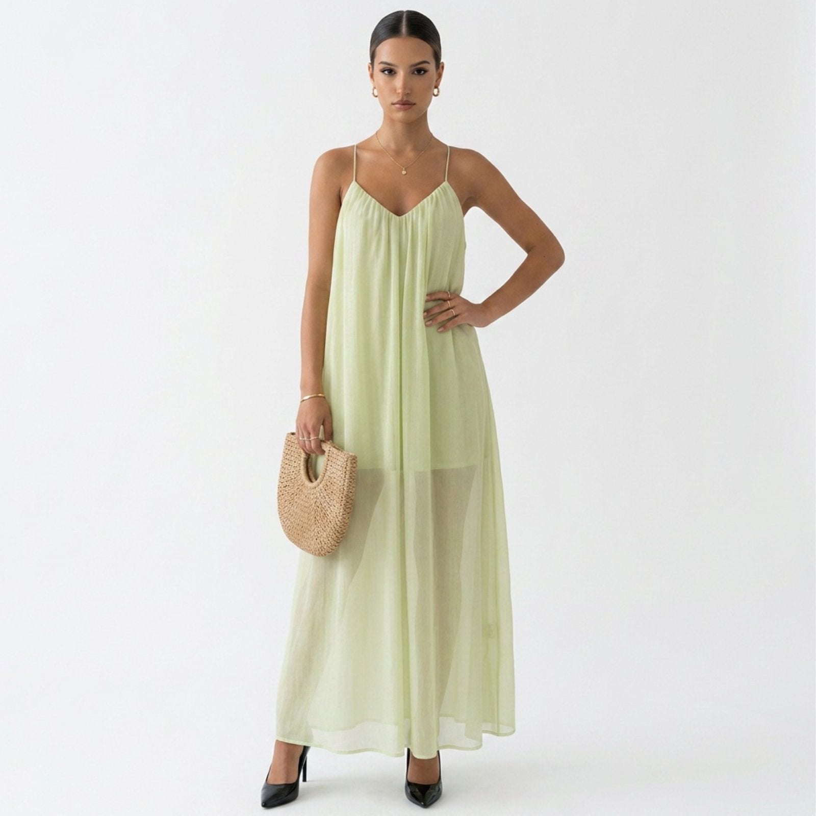 Woman wearing a light green dress holding a straw bag on a white background