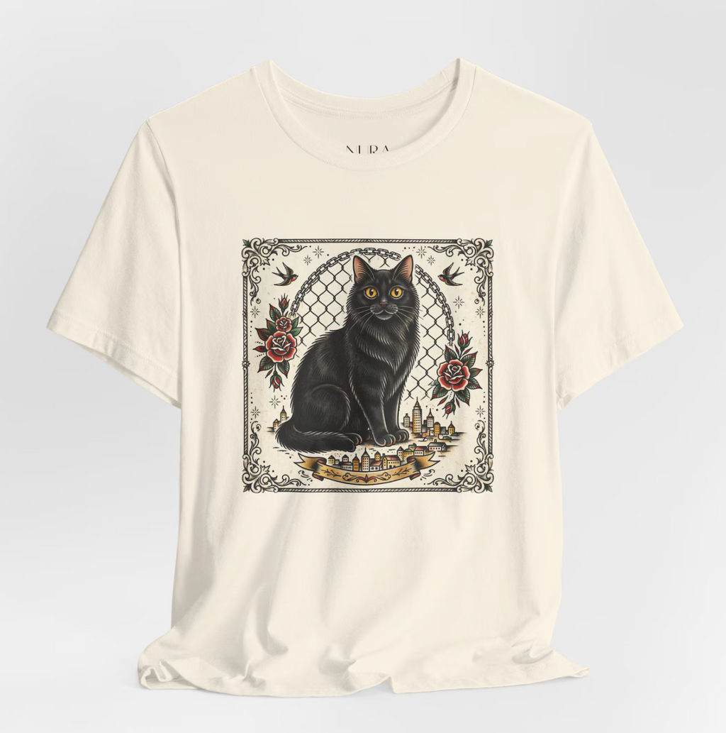 An off-white short-sleeve t-shirt with a central graphic print of a black cat sitting in front of a chain-link fence, surrounded by red roses and birds, on a light gray background.