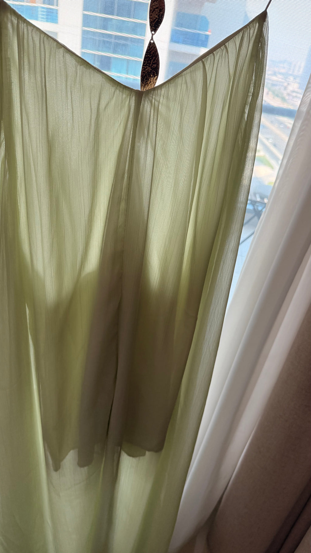 Light green curtain with white trim in front of a window with blue blinds.