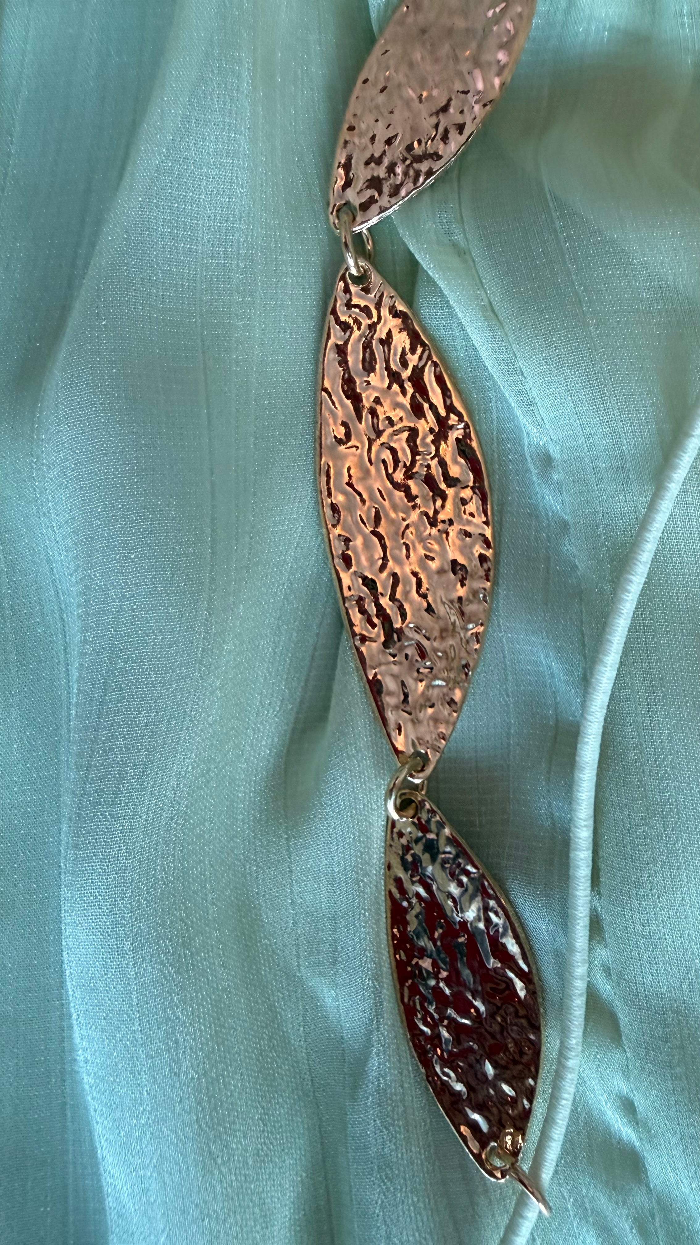 Bronze leaf-shaped pendant on a light green fabric background