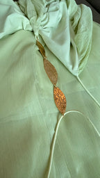 Gold leaf earring on a light green fabric background