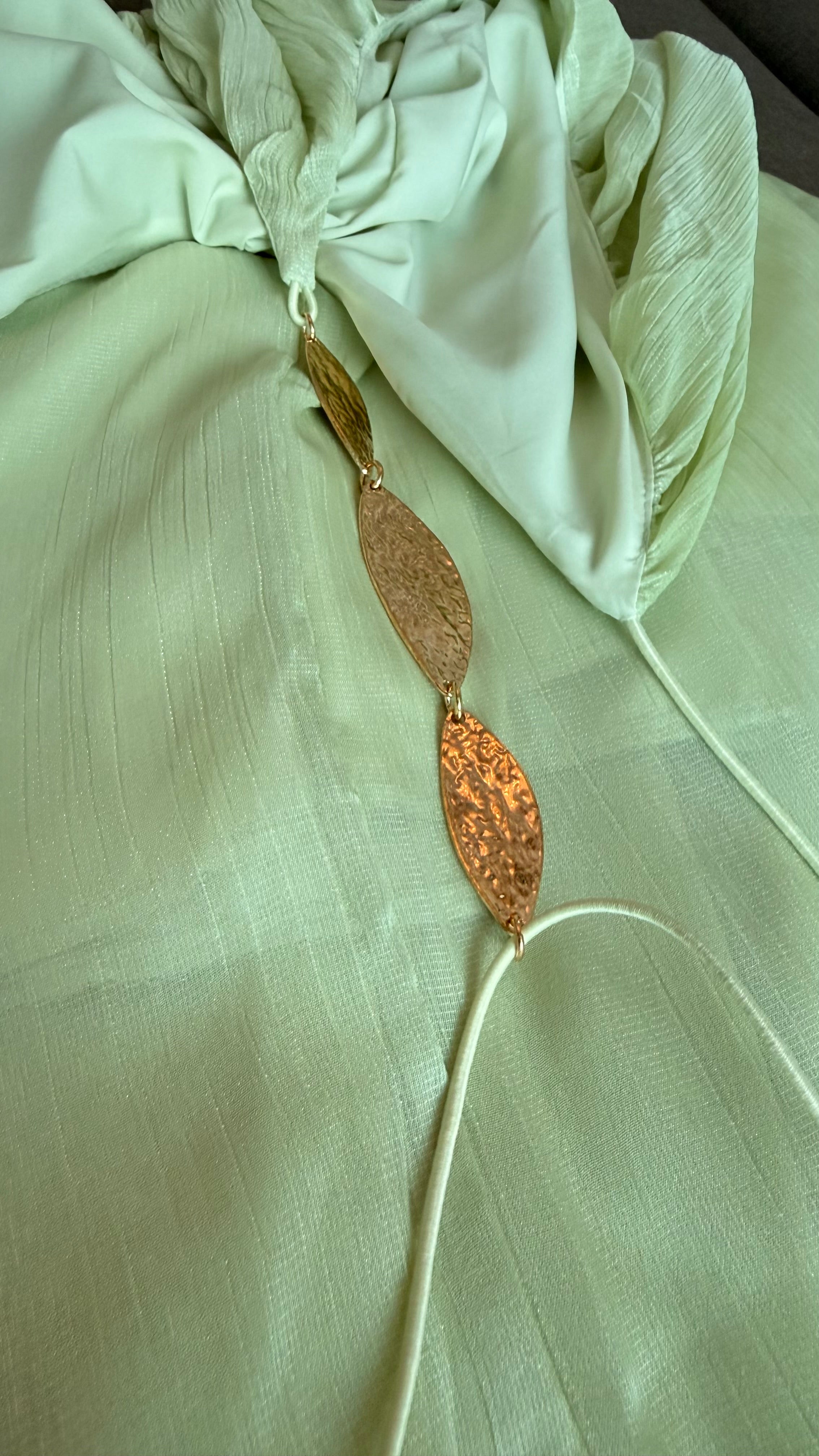 Gold leaf earring on a light green fabric background