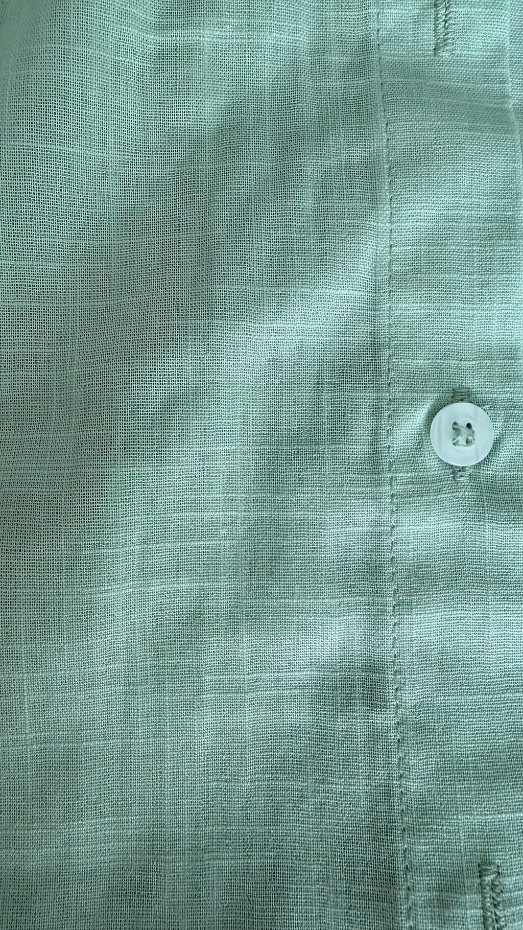 Close-up of a green shirt with a button, focusing on texture and color.