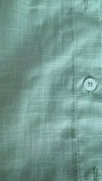 Close-up of a green shirt with a button, focusing on texture and color.