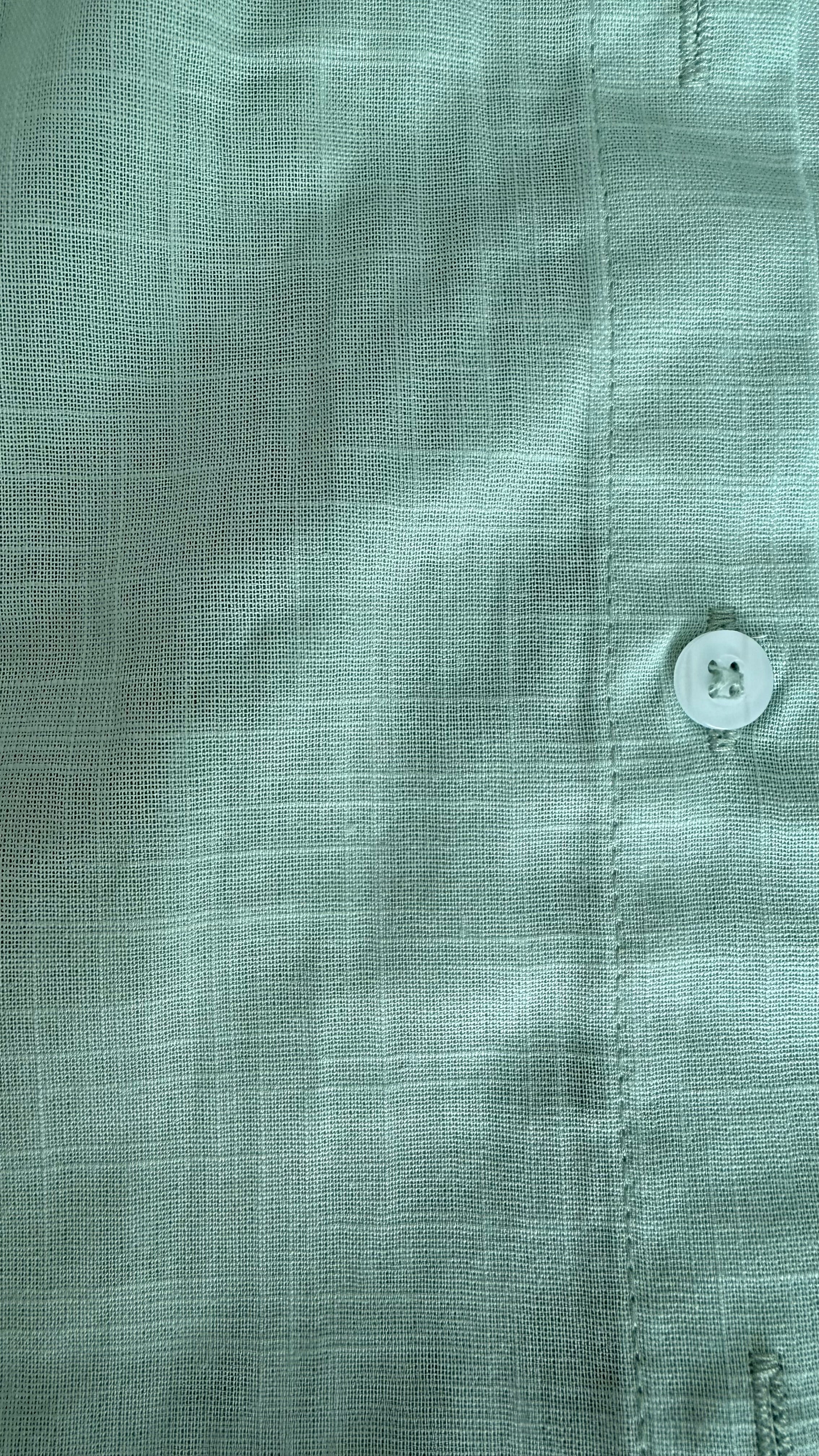 Close-up of a green shirt with a button, focusing on texture and color.