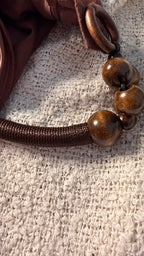 Close-up of a brown leather strap with wooden beads on a textured beige surface