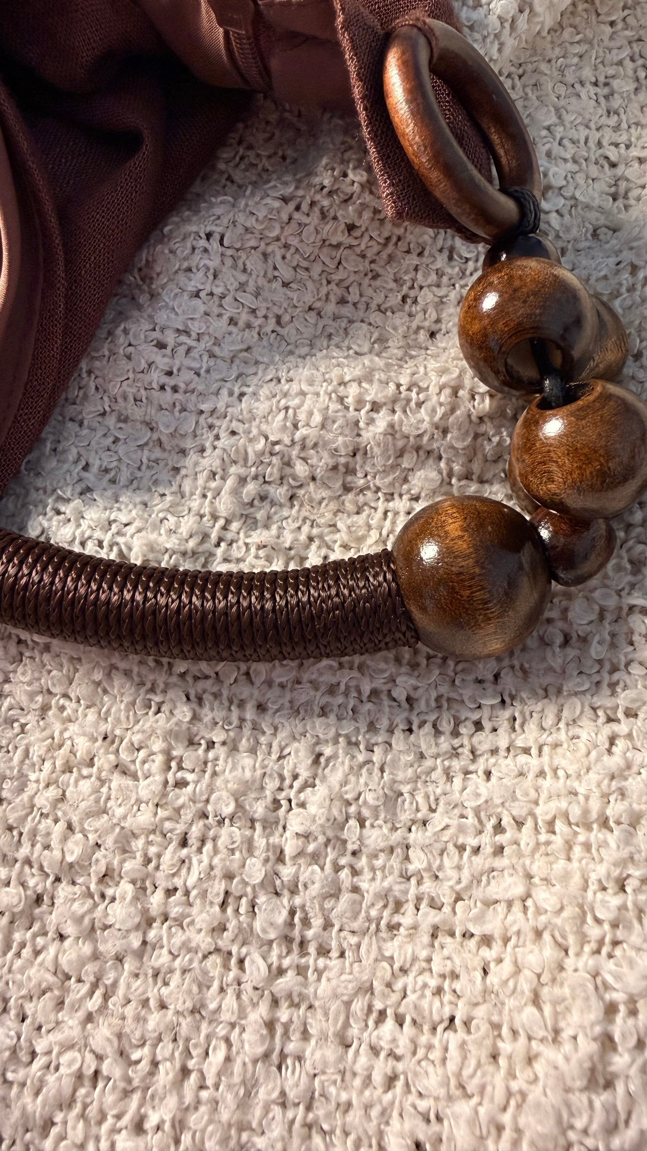 Close-up of a brown leather strap with wooden beads on a textured beige surface