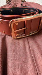 Close-up of a brown leather belt with a gold buckle on a textured surface.