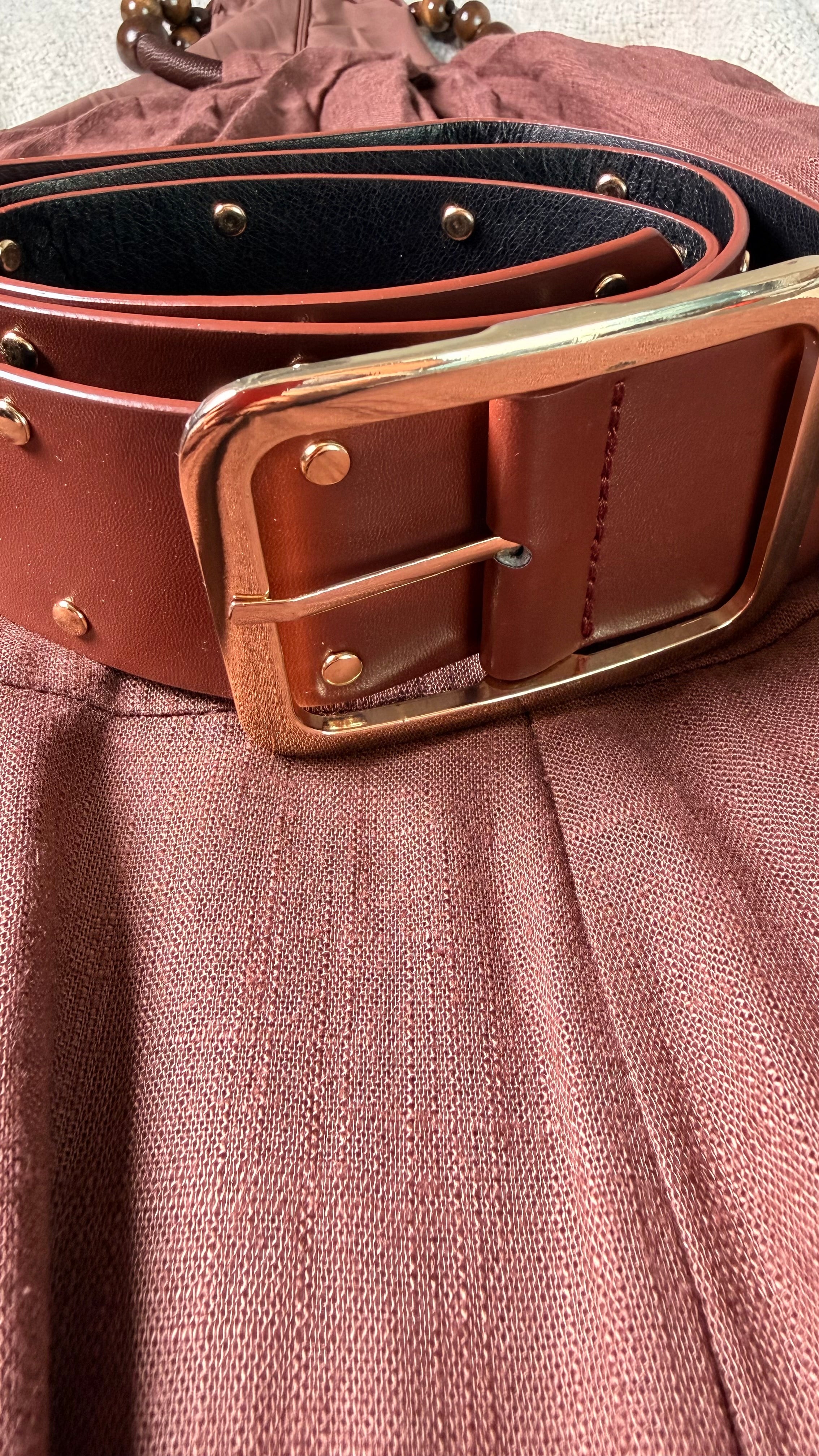 Close-up of a brown leather belt with a gold buckle on a textured surface.