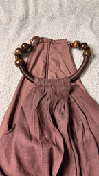 Brown dress with wooden beads on straps laid flat on a textured surface