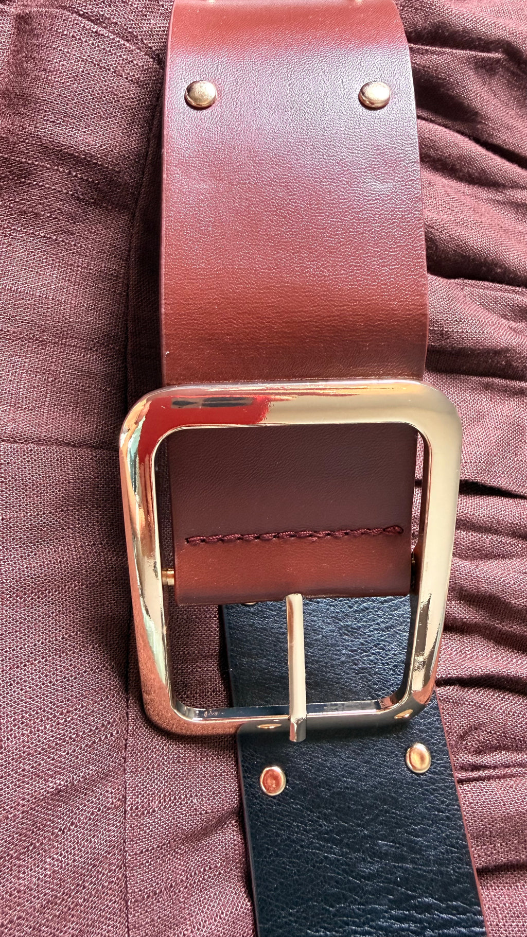 Brown leather belt with gold buckle on a textured surface