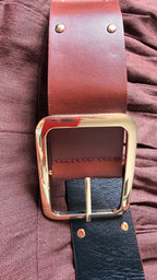 Brown leather belt with gold buckle on a textured surface