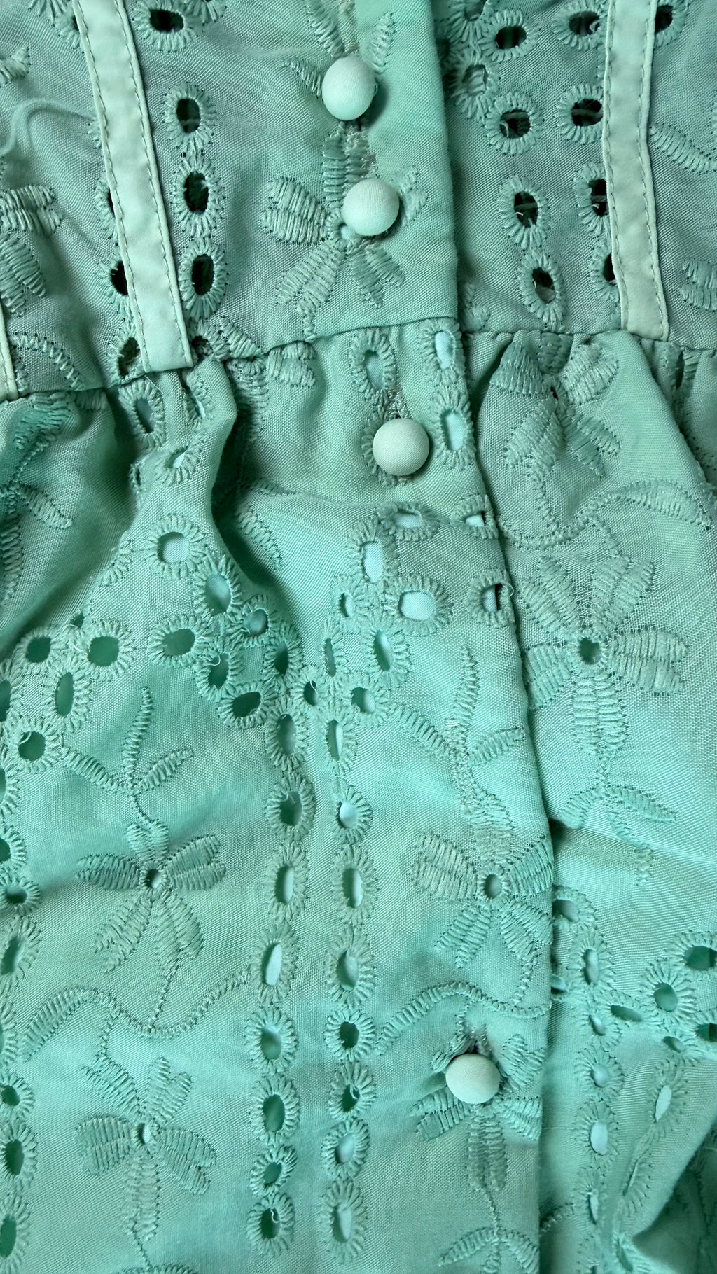 Close-up of a light green fabric with embroidered patterns and buttons.
