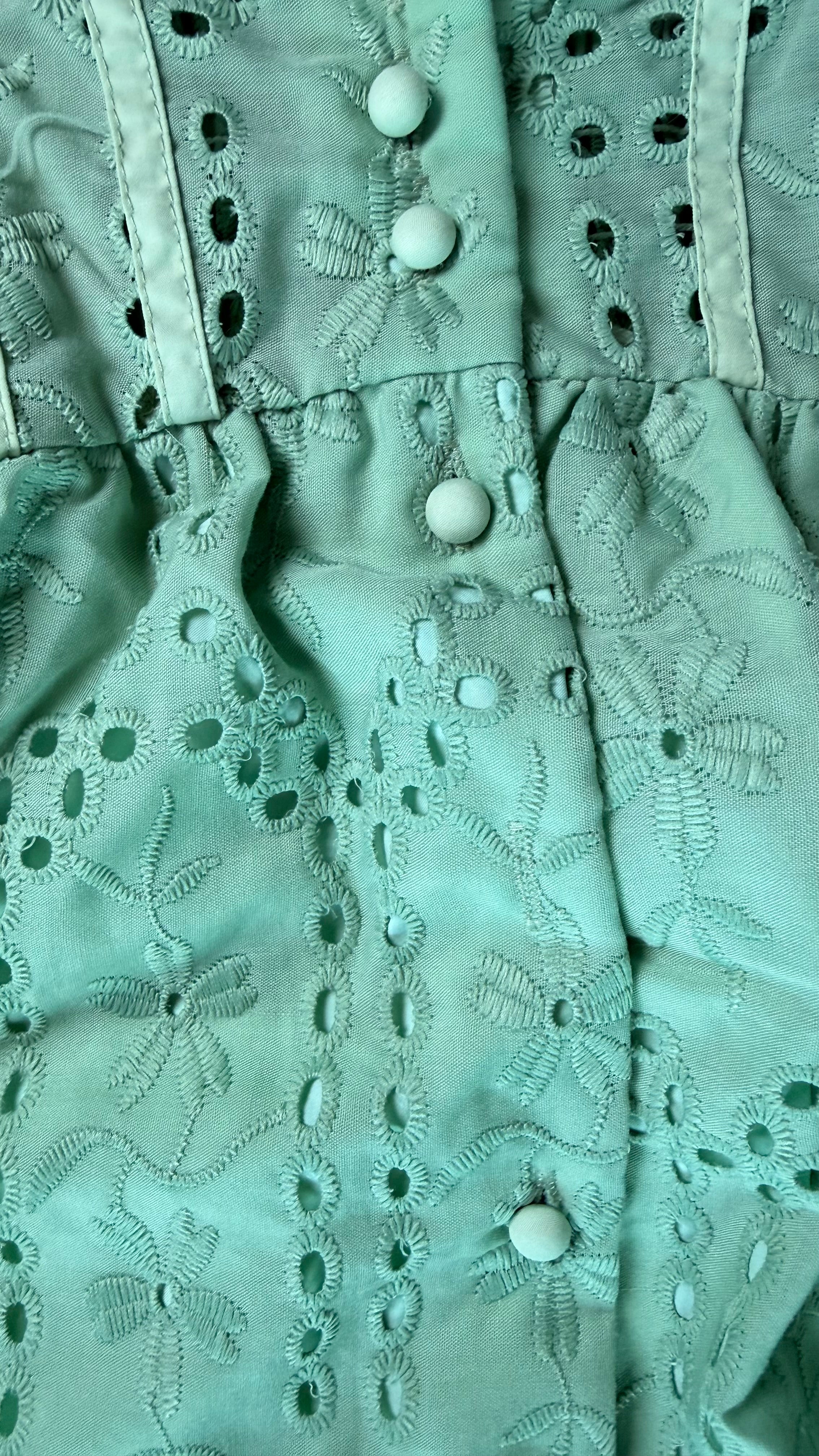 Close-up of a light green fabric with embroidered patterns and buttons.
