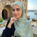 Woman wearing a light green hijab with a scenic background of a harbor.