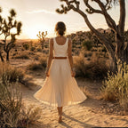 Woman in a flowing dress walking through a desert landscape with a sunset.
