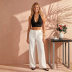 Woman wearing a black halter top and white pants standing against a beige wall.