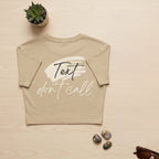 Beige t-shirt with 'Text don't call' text on a light wooden surface with decorative items.