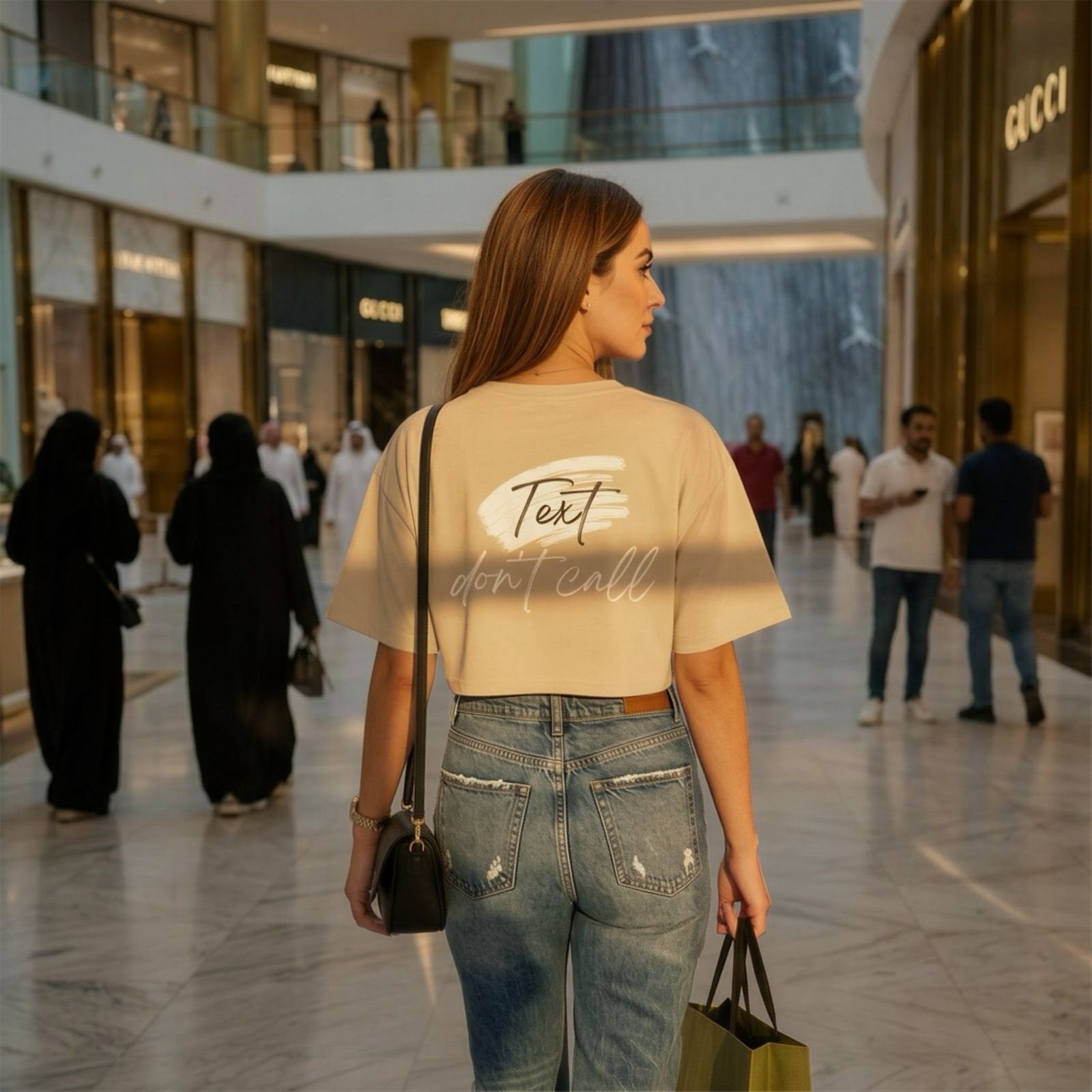 Woman walking in Dubai mall wearing a beige t-shirt with text and blue jeans.