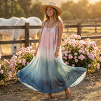 Woman in a long, colorful dress standing in a field with flowers and horses in the background.