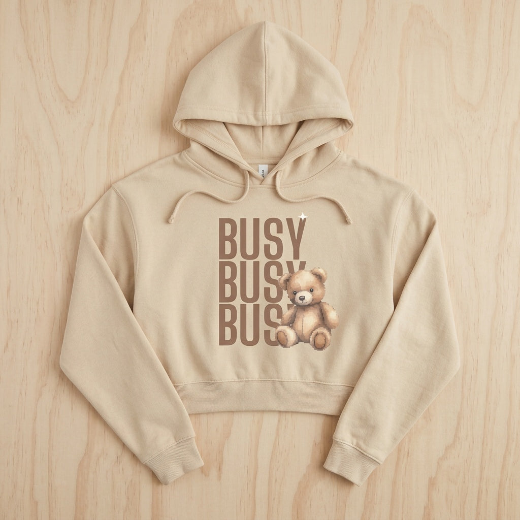 Beige hoodie with teddy bear and 'BUSY BUSY BUS' text on a wooden surface