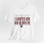 A white short-sleeve crewneck t-shirt with a graphic print on the front. The graphic is styled like a 'Certificate of Adoption' with the text 'I ADOPTED HIM NOW HE OWNS ME' in a dark red serif font, accented with a small dark red paw print and splatter design below.